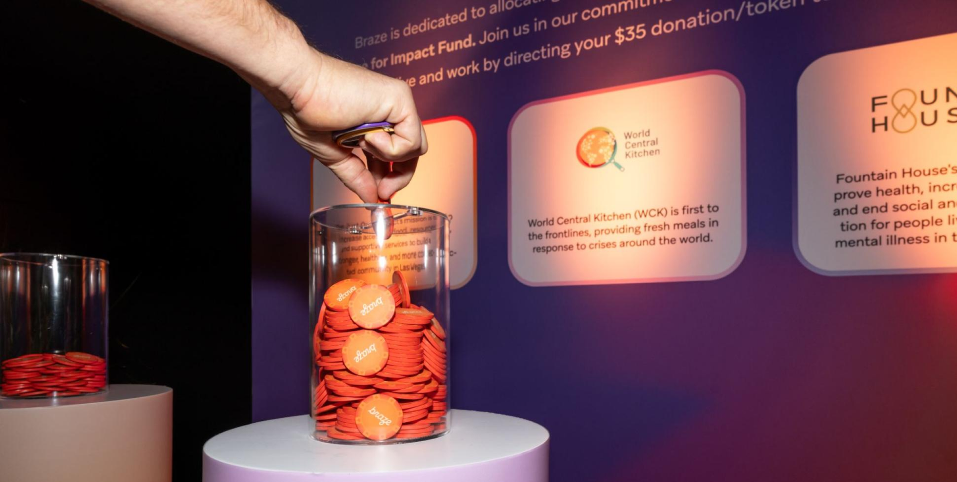 A hand drops an orange token into a clear container, part of a display for charitable donations to organizations like World Central Kitchen.