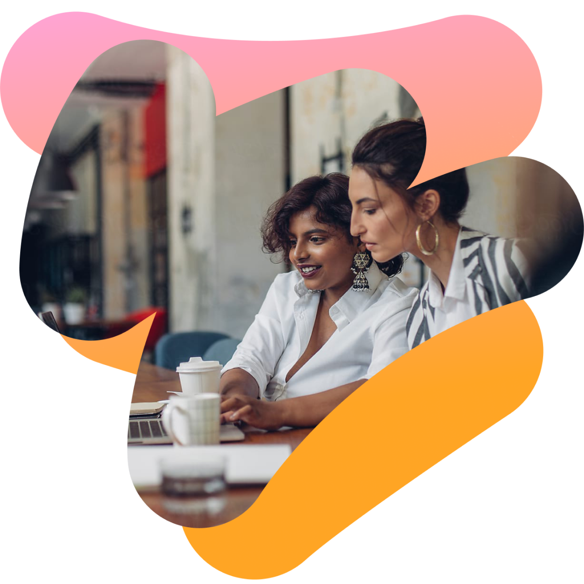 two women sit at a table looking at a laptop