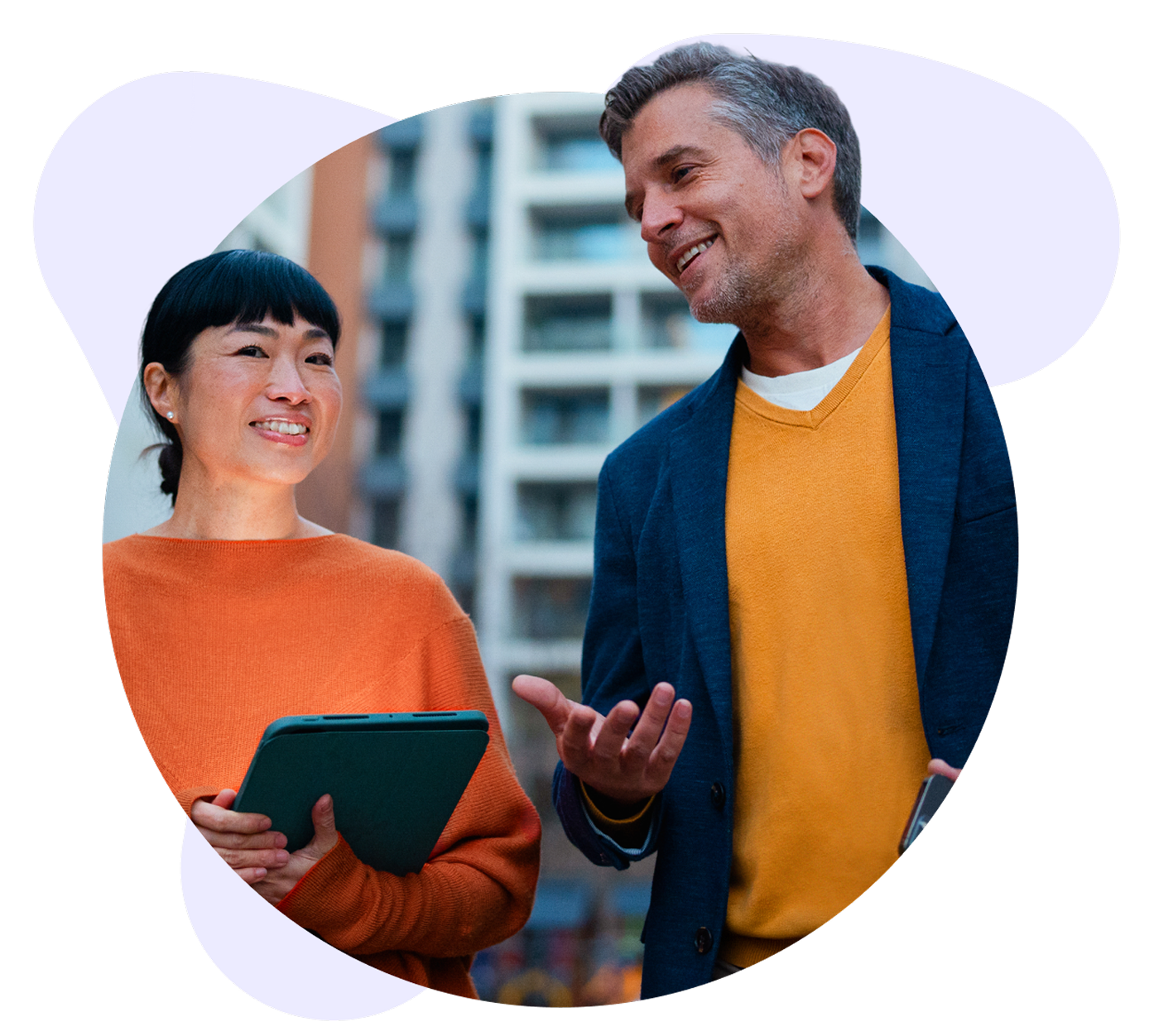 Smiling man and woman converse outdoors, the woman holding a tablet and the man gesturing.