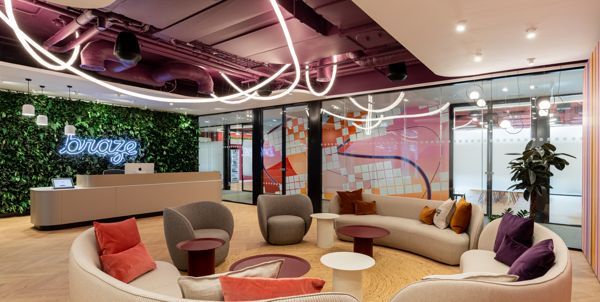 A modern office reception area with a green wall, a neon "braze" sign, and colorful curved seating.