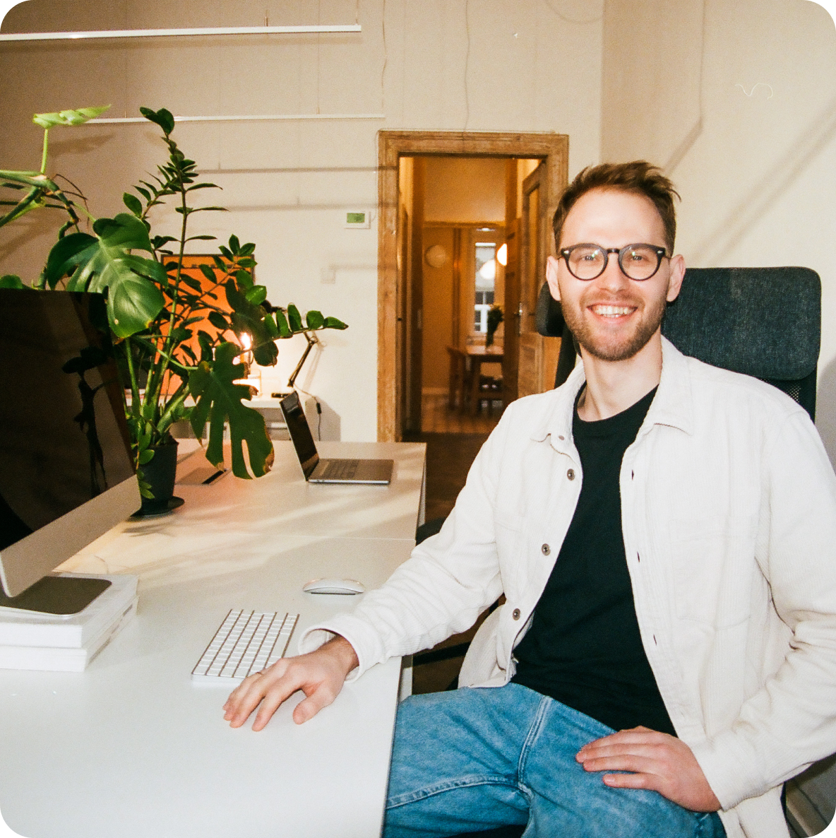 a man wearing glasses sits at a desk with a keyboard