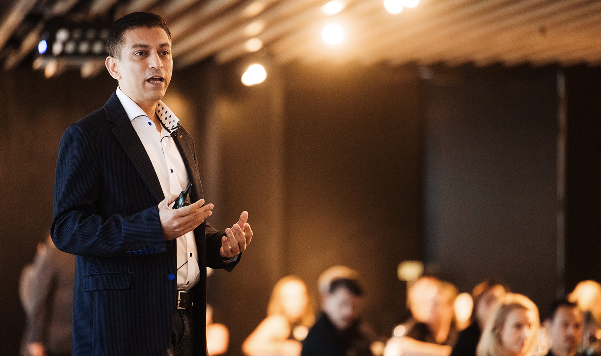 Man in a suit jacket speaking and gesturing to an audience.