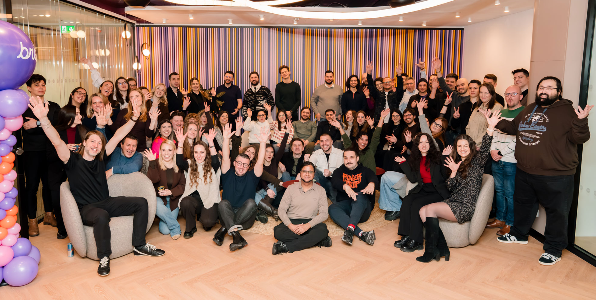 A large group of smiling people waving and posing for a photo in a modern office.